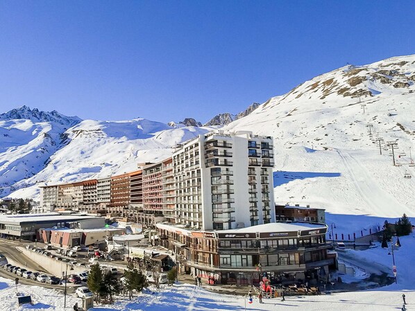 Un hôtel à plusieurs étages, avec un télésiège visible en arrière-plan, entouré de montagnes enneigées.