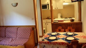 Zona pranzo con tavolo imbandito per quattro, cucina sullo sfondo e televisione montata a parete.