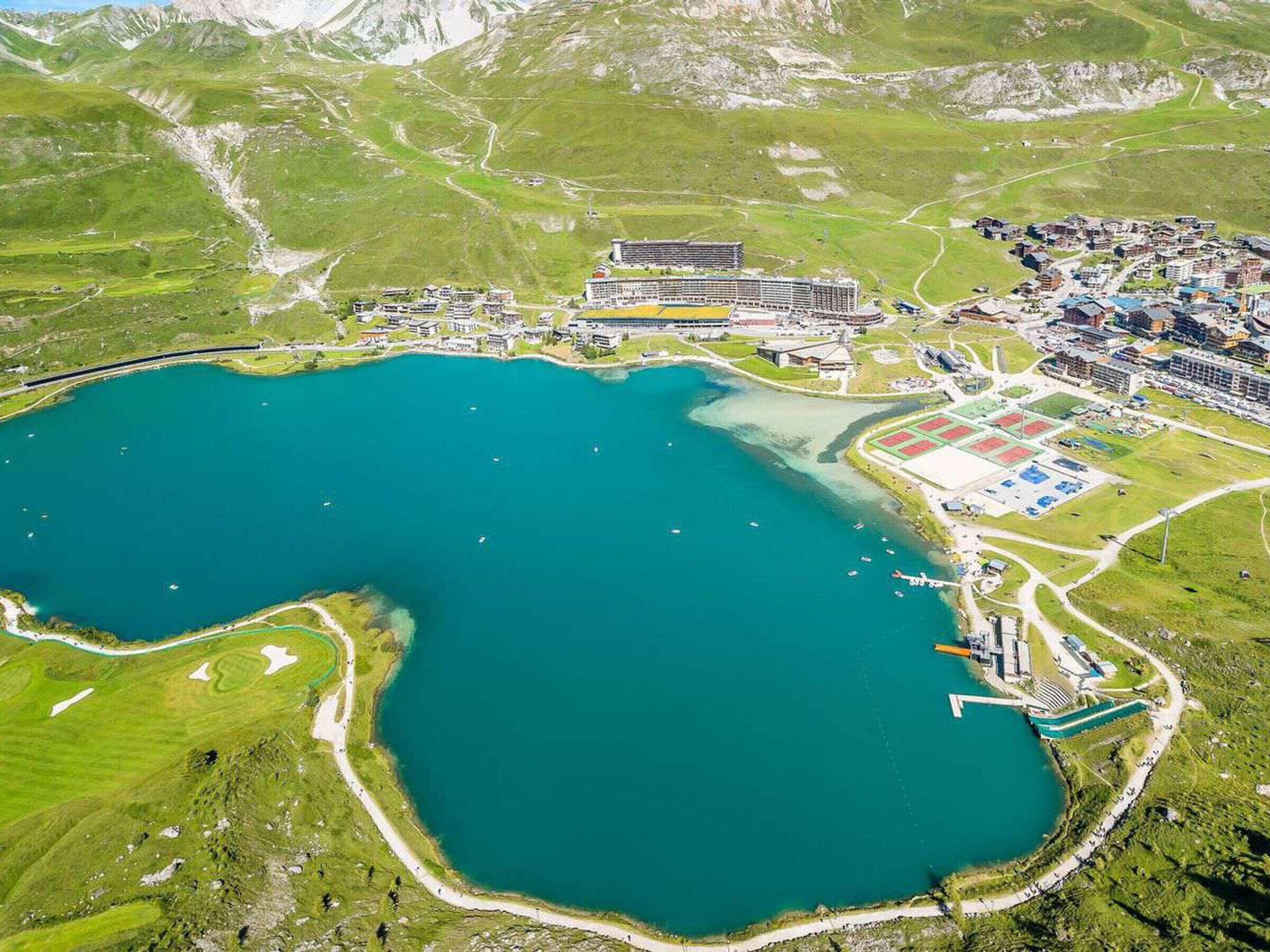 Vista aérea de una zona costera con una masa de agua, un conjunto de edificios y un campo deportivo.