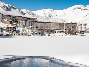 Een bergresort bedekt met sneeuw, met meerdere gebouwen, waaronder een groot hotel met balkons en een skilift zichtbaar op de achtergrond.