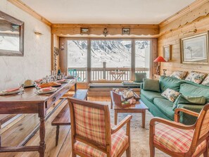 A cozy cabin interior with a dining area, a green sofa, and a view of snow-capped mountains. - 3* Apartment cozy, comfortable, 7 pers, lake view (Tignes)