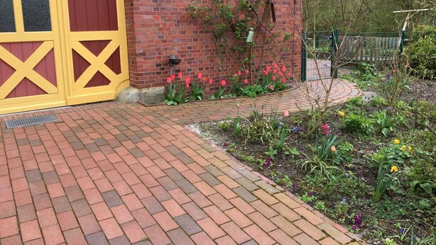 A brick building with a yellow door and a garden with various plants and flowers. - Dirkshof 2 West, Germany (Varel)