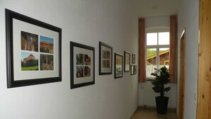 A hallway with framed pictures on the wall, a potted plant, and a window with curtains. - Dirkshof 2 West, Germany (Varel)