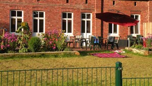 A brick building with a red-tiled roof, outdoor seating, and a garden with flowers. - Dirkshof 2 West, Germany (Varel)