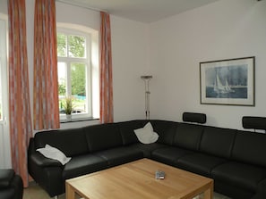 A living room with a black leather sofa, a wooden coffee table, a floor lamp, and a painting on the wall. - Dirkshof 2 West, Germany (Varel)