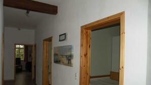 A hallway with wooden doors leading to a bedroom with a bed. There is a poster on the wall and a television in the adjacent room. - Dirkshof 2 West, Germany (Varel)