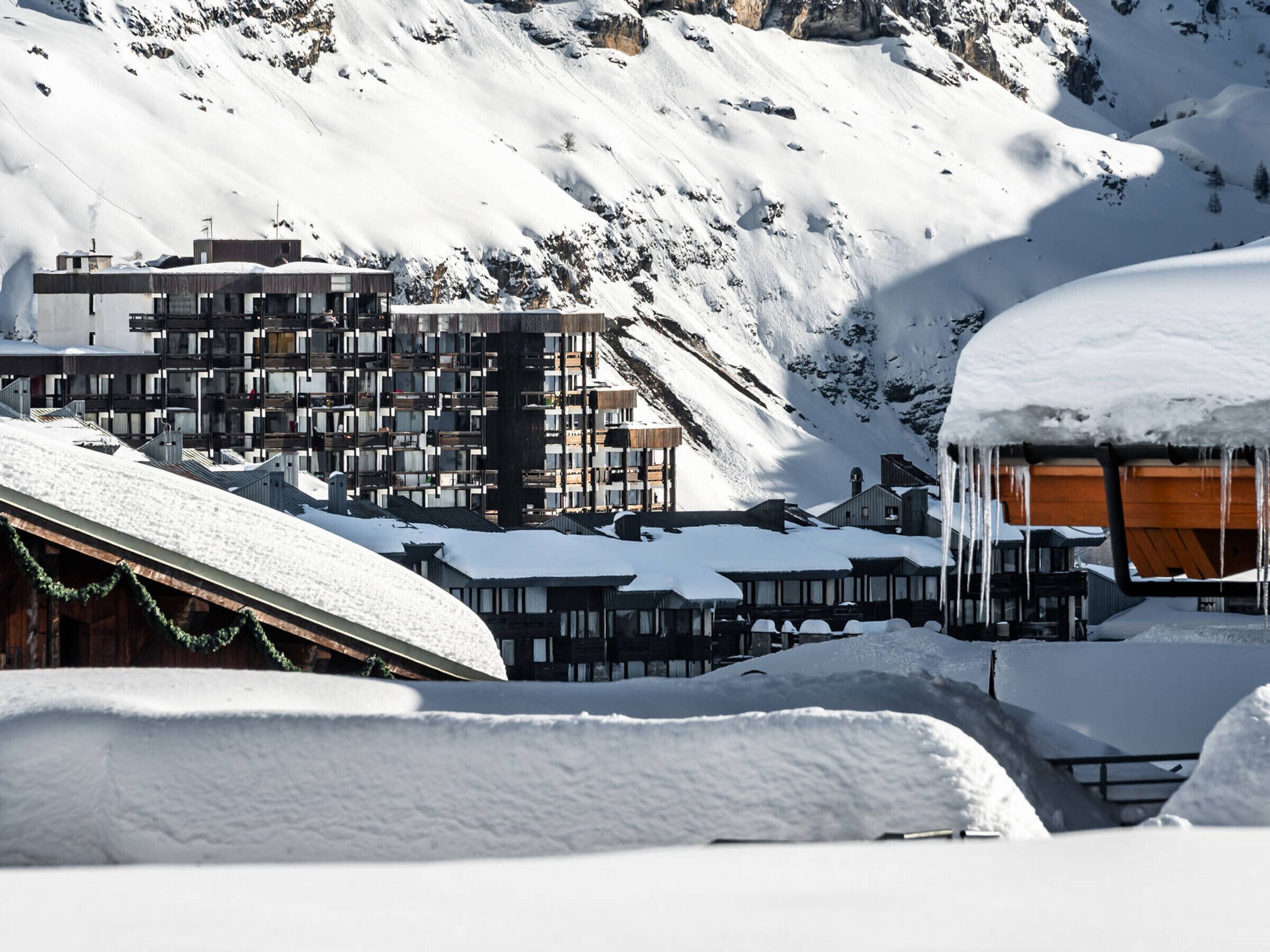 A snow-covered mountain village with modern and traditional buildings, including a wooden structure with a sloped roof.