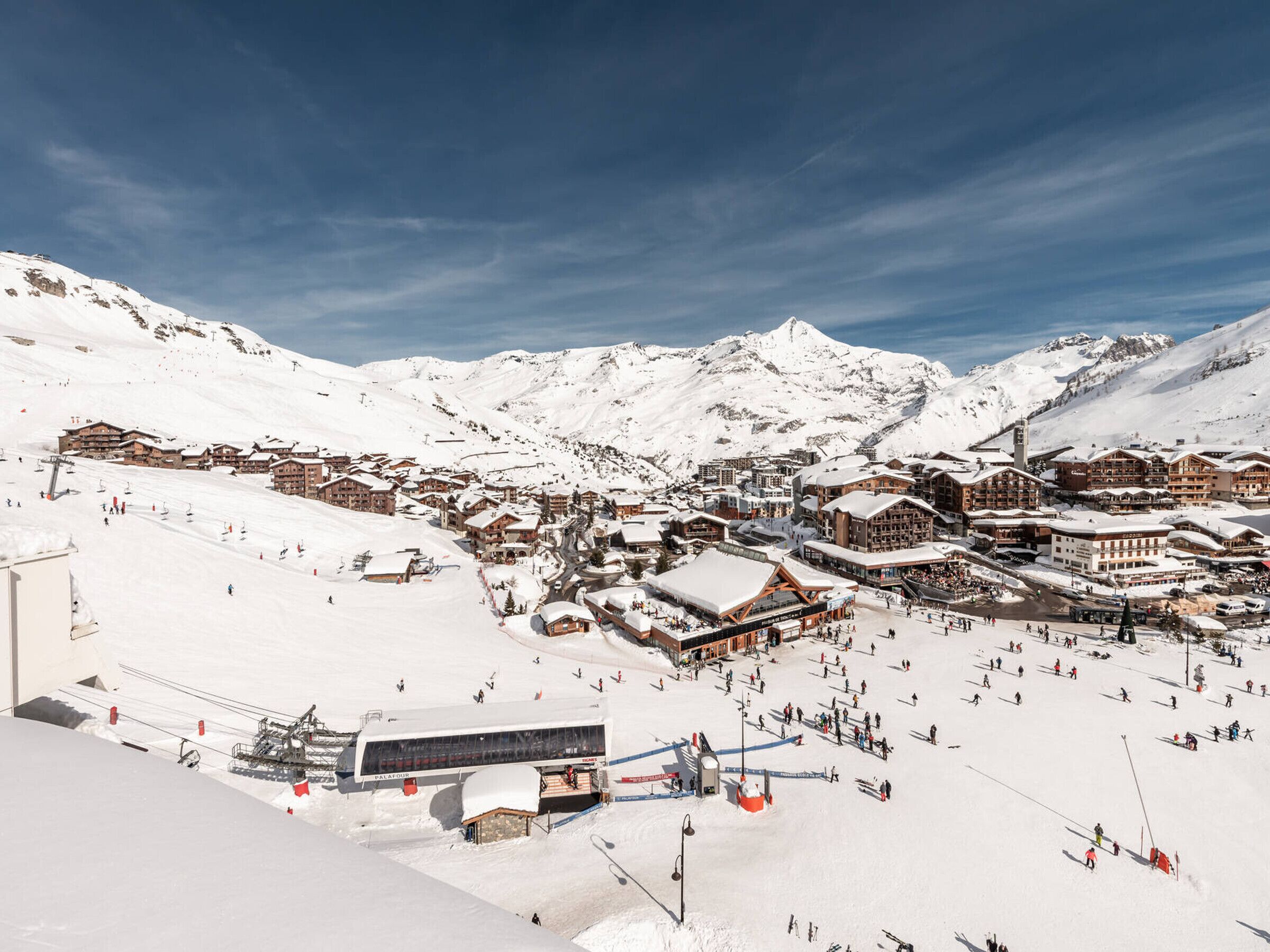 Une ville de montagne enneigée, avec des pistes de ski, des bâtiments et un ciel dégagé.