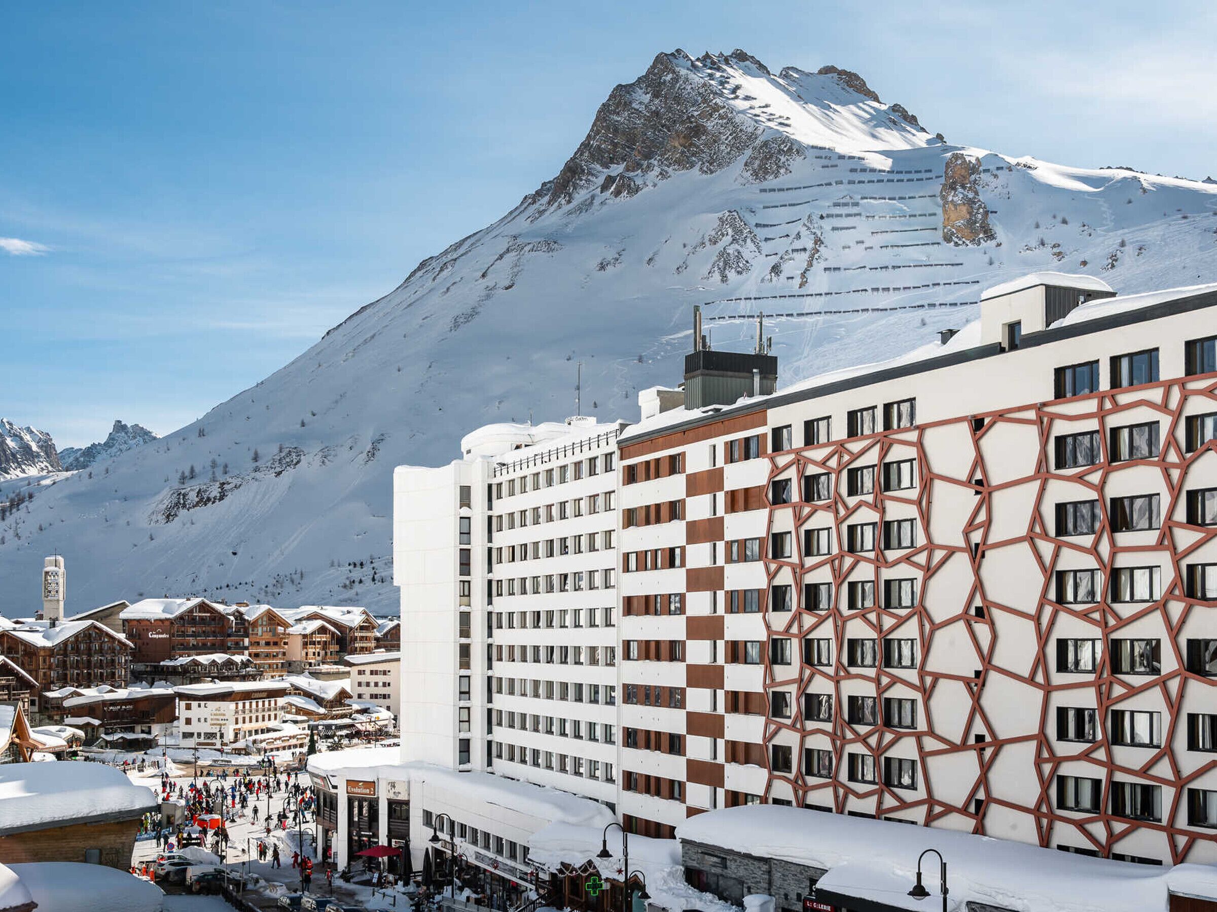 A hotel with a modern facade, multiple floors, and a view of a snow-covered mountain.