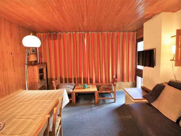 Une pièce chaleureuse avec un plafond en bois, un canapé, une petite table avec une théière et un téléviseur fixé au mur.