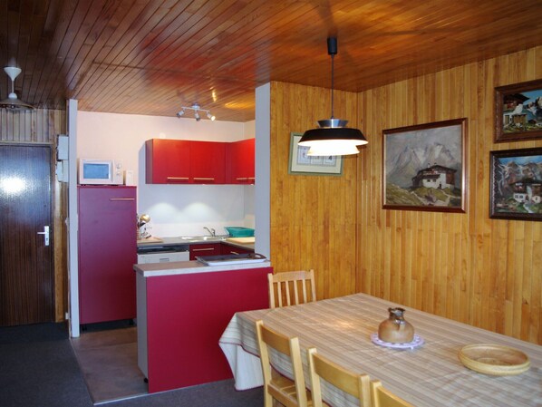 Eine kleine Küche mit roten Schränken, einem Holztisch und einem Bild an der Wand.