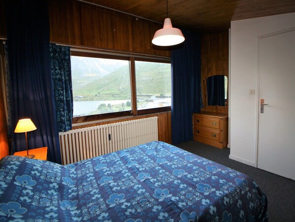 Une chambre à coucher comprenant un lit, une commode et une fenêtre donnant sur un lac et des montagnes.