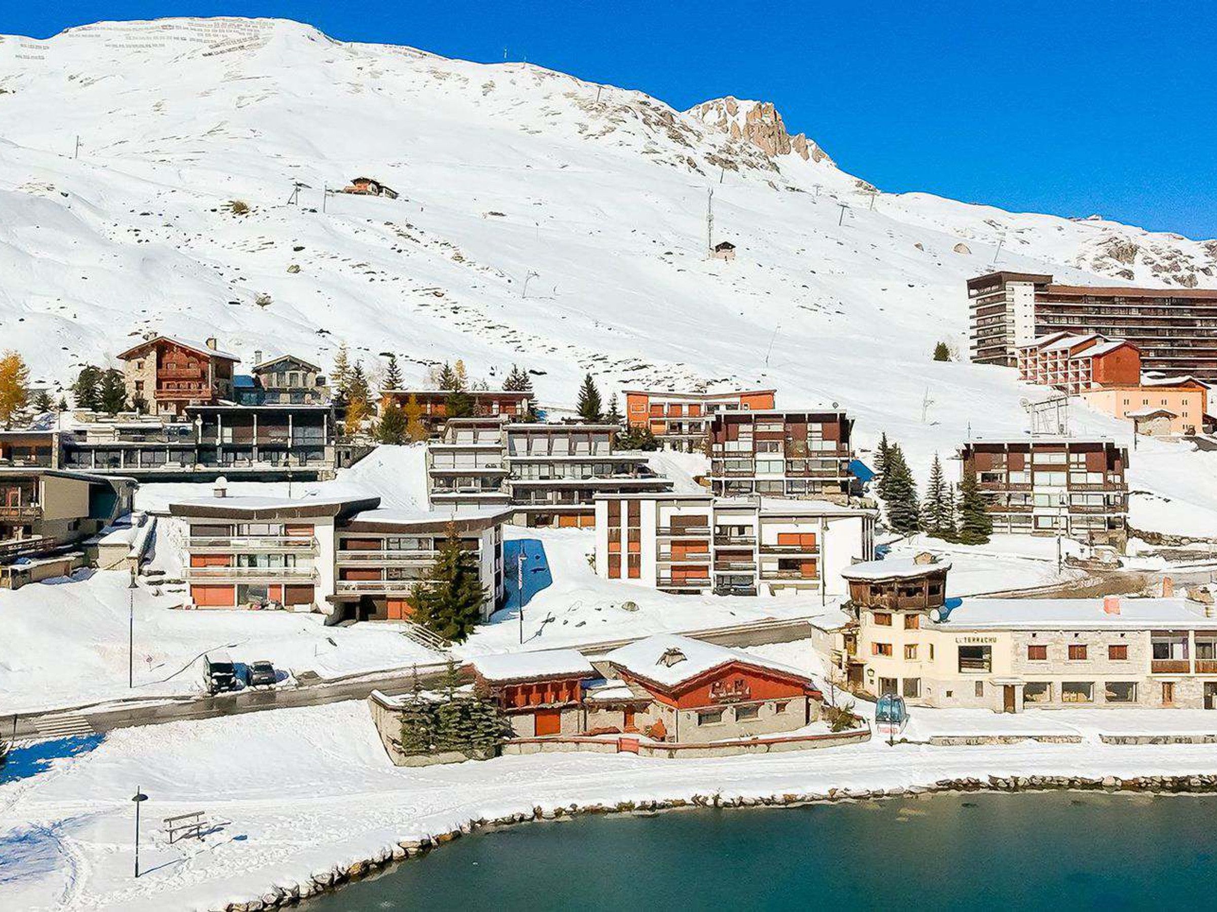 Une ville de montagne enneigée, avec des bâtiments modernes, un petit lac et un ciel bleu dégagé.