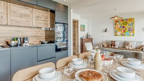 Una cucina moderna con mobili grigi e dettagli in legno, una zona pranzo con un tavolo apparecchiato per sei persone e un quadro astratto dai colori vivaci appeso al muro.