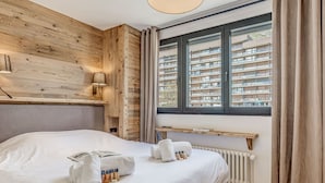 Camera d'albergo con testiera in legno, un letto grande con lenzuola bianche, un comodino con una lampada e una finestra che offre vista su un edificio residenziale.