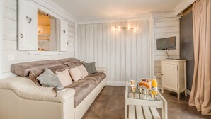 A cozy living room with a beige sofa, a glass coffee table with breakfast items, a TV on a wooden cabinet, and a mirror on the wall. - Renovated comfy studio 4 ppl with balcony in Tignes (Tignes)