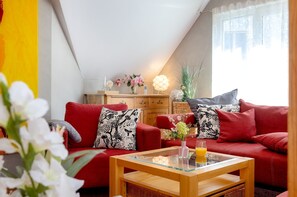 A cozy living room with a red sofa, a wooden coffee table, and a vase with flowers.