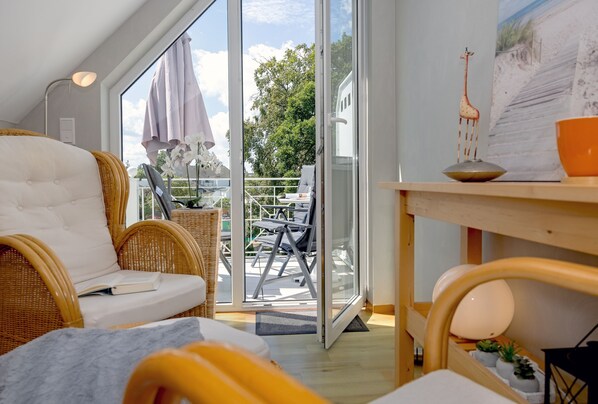A modern, well-lit room with a large sliding glass door leading to an outdoor area. Inside, there is a comfortable seating area with a sofa and chairs, a small table with a lamp, and a decorative giraffe figurine.