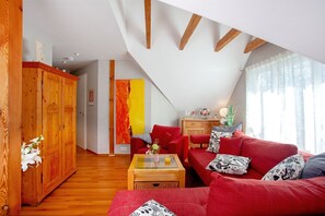 Een moderne woonkamer met een rode bank, houten kasten en een glazen salontafel.