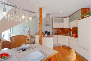 Eine moderne Küche mit weißen Schränken, Holz Arbeitsplatten und einem Essbereich mit Korbstühlen und einem Tisch für zwei Personen.