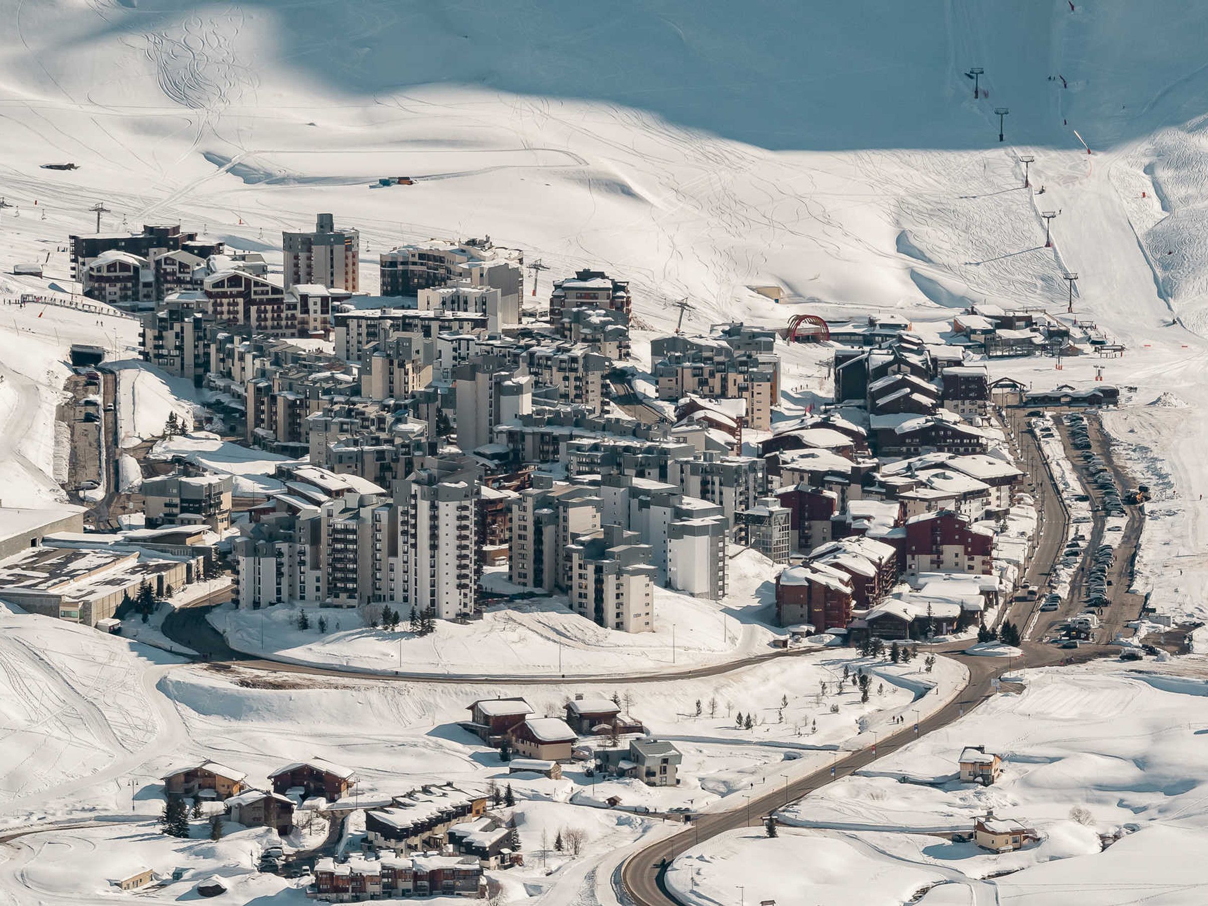 Een besneeuwde bergstad met meerdere gebouwen, wegen en skiliften.