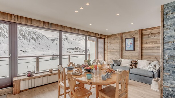 A dining area with a wooden table, chairs, and a view of snow-covered mountains. - Premium 3-room apartment, lake view, 6 pers., WIFI, in Tignes (Tignes)