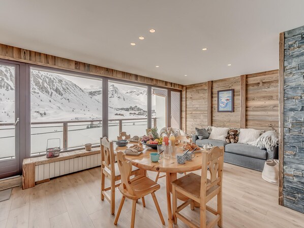 A dining area with a wooden table, chairs, and a view of snow-covered mountains.