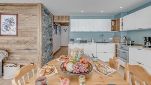 A modern kitchen with white cabinets, a stone accent wall, and a dining area with a wooden table set for a meal. - Premium 3-room apartment, lake view, 6 pers., WIFI, in Tignes (Tignes)