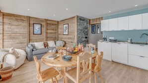 A modern living room with a wooden floor, a round wooden dining table, and a grey sofa. There is a kitchen area with white cabinets and a blue backsplash. - Premium 3-room apartment, lake view, 6 pers., WIFI, in Tignes (Tignes)