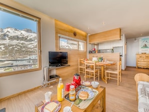 Cozinha moderna com área de refeições, televisão e vista para montanhas nevadas.