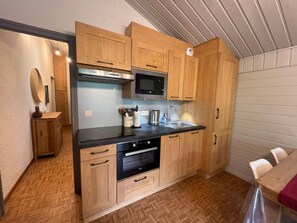 A compact kitchen with wooden cabinets, a microwave, an oven, and a sink.