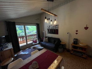A room with a bed, a sofa, a dining table, and a view of a balcony.