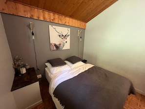 A bedroom with a bed, a wooden ceiling, a wall-mounted light fixture, and a framed picture. - Cozy apartment for 4 with balcony and garage in Châtel (Châtel)