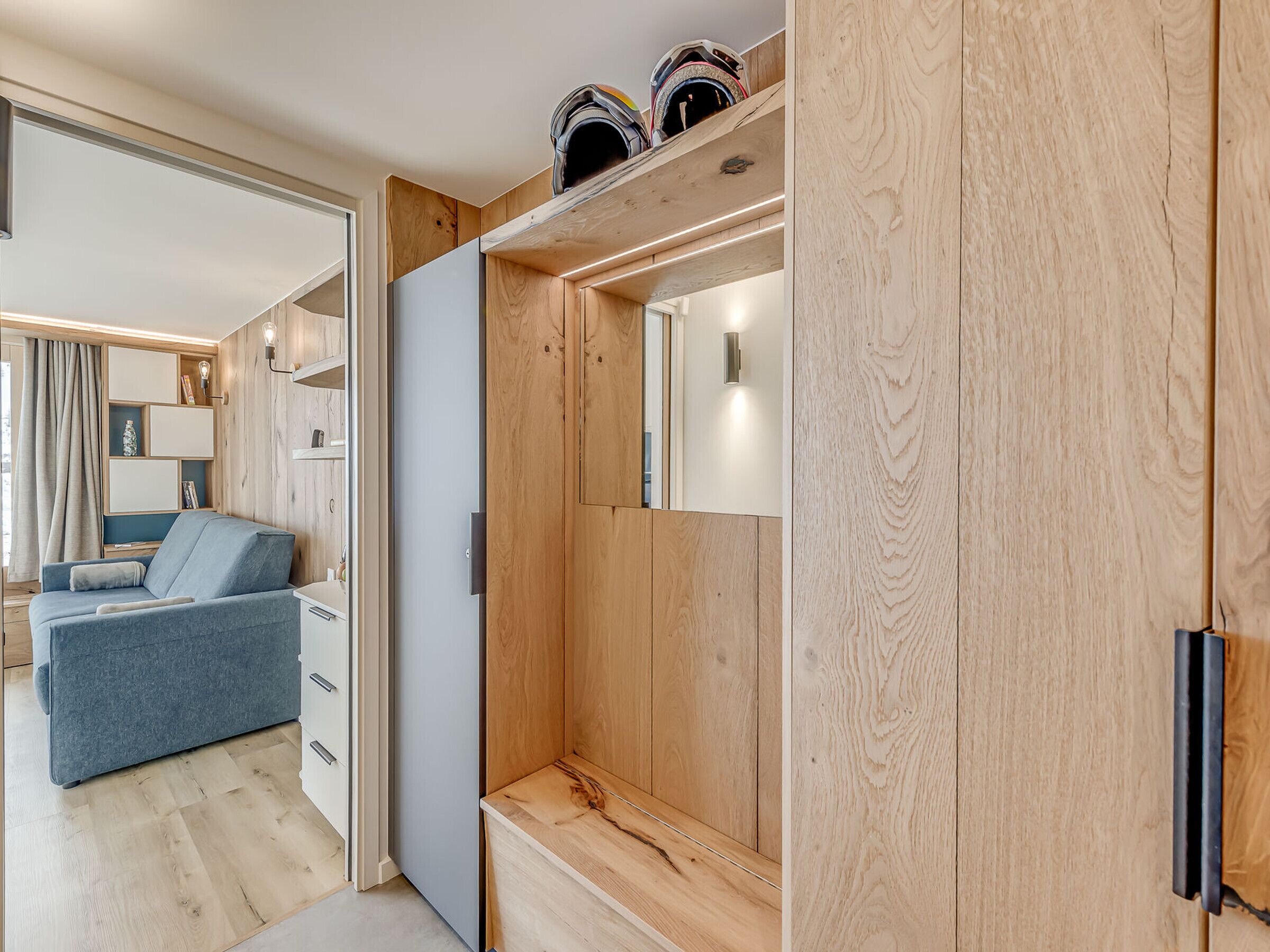 Une pièce moderne et bien éclairée, avec une armoire en bois, un canapé bleu et une bibliothèque intégrée.