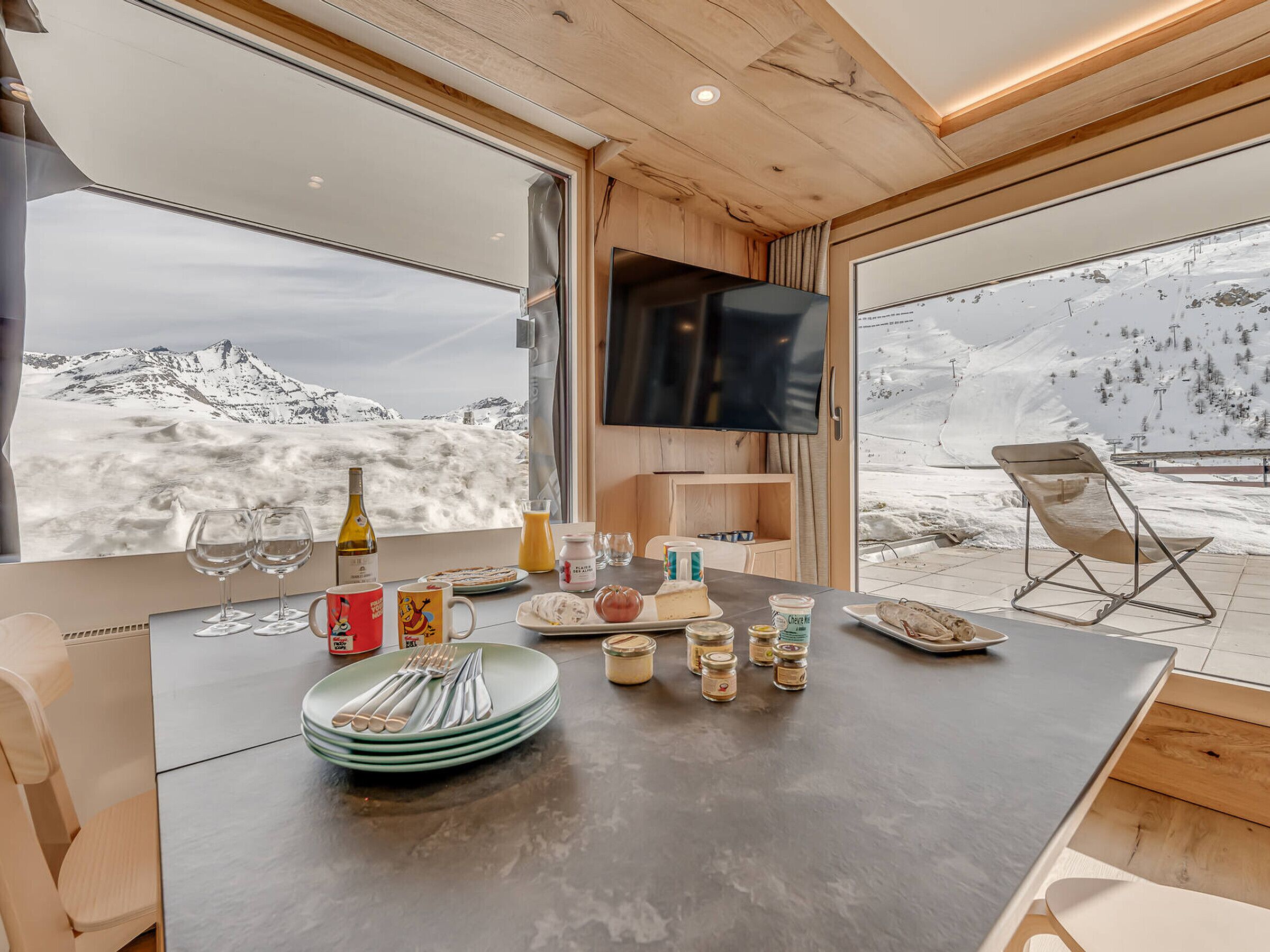A modern interior with a dining area, a TV, and a view of a snowy mountain landscape.