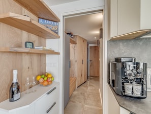 A modern kitchen with wooden shelves, a wine bottle, glasses, and a coffee machine.