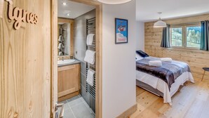 A modern bedroom with a wooden floor, a bed with a blanket, a bedside table, and a window with curtains. - Premium 4* Apartment Ski-in/Ski-out with SPA and Parking (Tignes-Les Boisses)