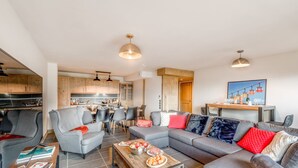 A modern living room with grey sofas, a wooden coffee table, and a kitchen in the background. - Premium 4* Apartment Ski-in/Ski-out with SPA and Parking (Tignes-Les Boisses)