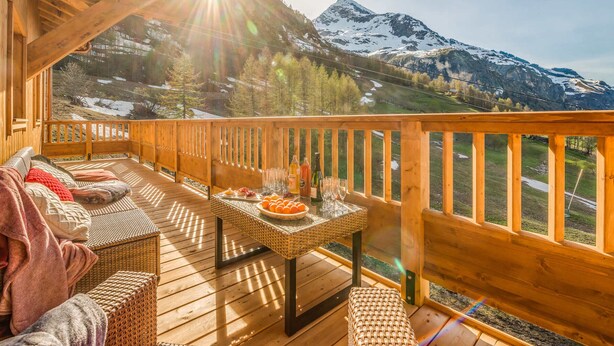 A wooden deck with a view of snow-capped mountains, a wicker sofa, and a table with drinks and snacks. - Premium 4* Apartment Ski-in/Ski-out with SPA and Parking (Tignes-Les Boisses)