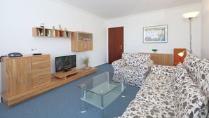A modern living room with a glass coffee table, wooden entertainment unit, and patterned sofa. - App. Arius 10, Germany (Sylt)