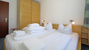 A hotel room with a neatly made bed, a wooden wardrobe, and a small table with towels. - App. Arius 10, Germany (Sylt)
