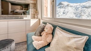 Una stanza accogliente con un divano, un orsetto e vista su una montagna innevata.