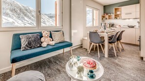Un soggiorno moderno con un divano blu, un orsetto di peluche e un'area pranzo con un tavolo apparecchiato per due.