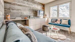 Un soggiorno accogliente con un divano blu, un tavolino con degli snack, una finestra con vista innevata e una parete in legno.