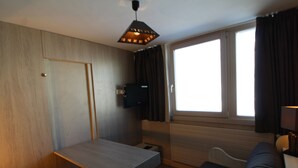 A compact room with a wooden door, a small table, a sofa, a TV mounted on the wall, and a window with curtains. - Renovated Studio for 2 - Tignes (Tignes)