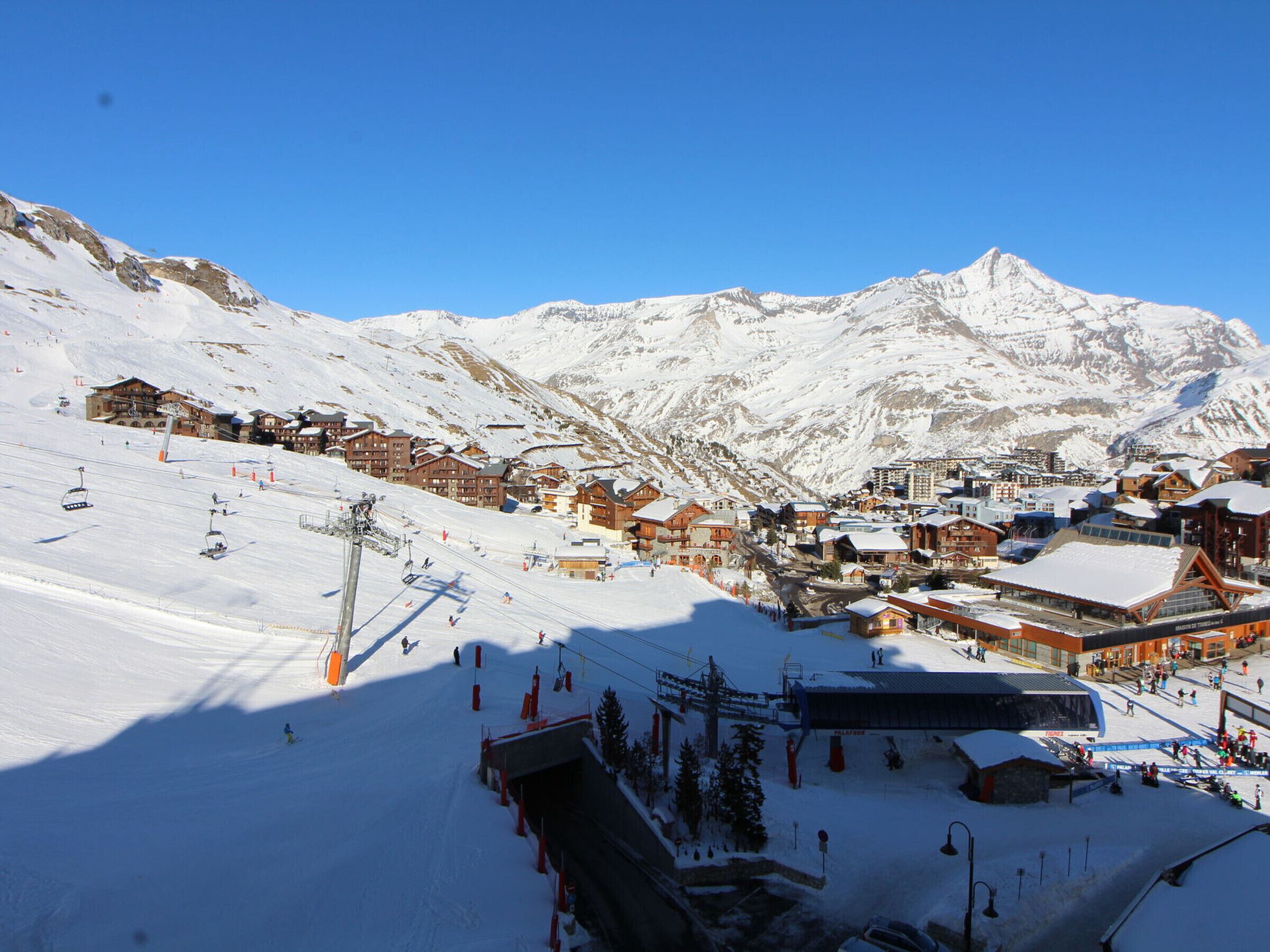 A snow-covered mountain town with ski lifts, wooden buildings, and a clear blue sky.
