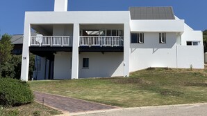 A modern two-story house with a flat roof, a balcony on the upper floor, and a chimney.