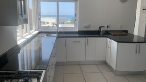 A modern kitchen with white cabinets, a black countertop, a stainless steel sink, and a gas stove.
