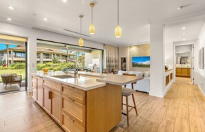 A modern kitchen with wooden cabinets, a central island, pendant lighting, and a view of the outdoor area.