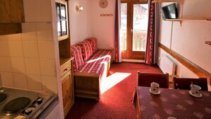 Una habitación compacta con kitchenette, una cama con colcha estampada de motivos rojos, una mesa de comedor con mantel temático de corazones y un televisor montado en la pared.